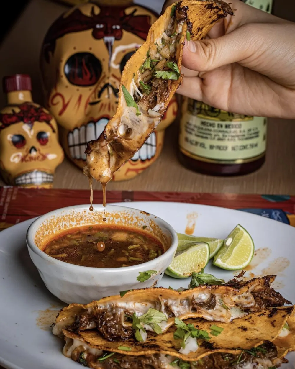Birria taco held over a bowl of consomé