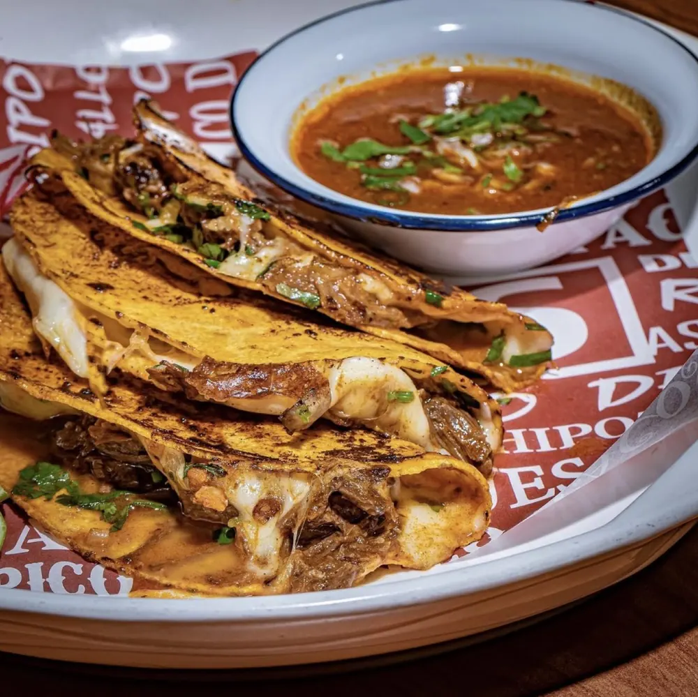 Quesa birria tacos on Sunrise Tacos paper with consomé